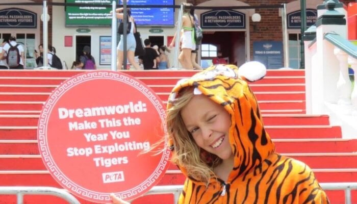 A child dressed in a tiger onesie outside Dreamworld with a sign reading: "Dreamworld: Make This The Year You Stop Exploiting Tigers".