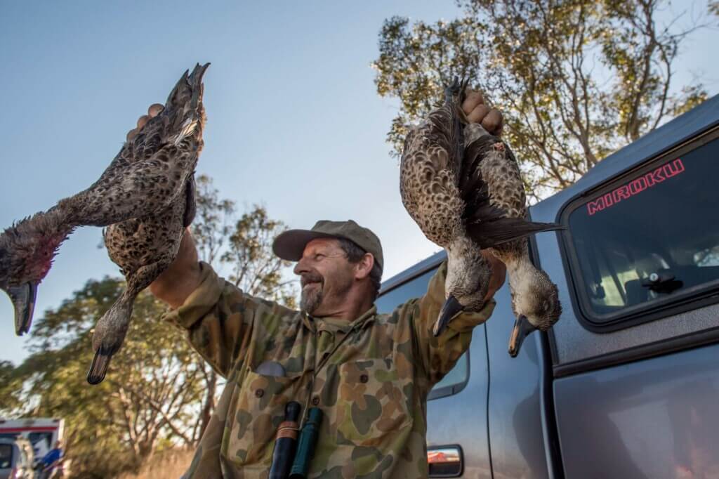 A photo of a hunter with dead ducks.