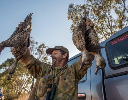 A photo of a hunter with dead ducks.