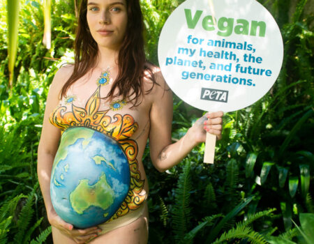 Eliza stands with a sign reading: "Vegan for animals, my health, the planet, and future generations."