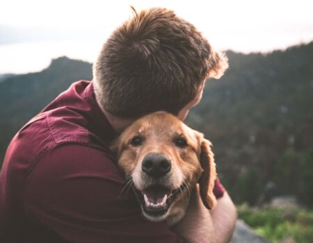 A person with short hair hugs a smiling dog