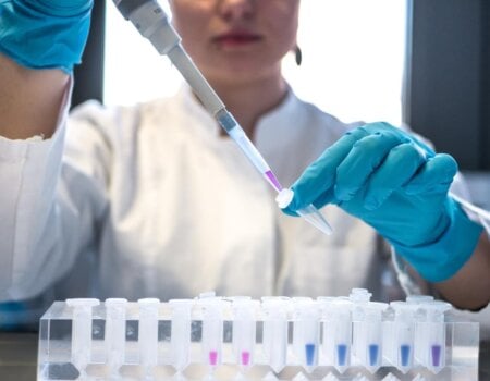 Female scientist pipetting colored chemicals into a tube.